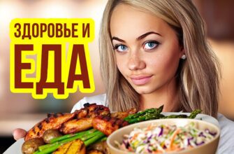 Изображение представляет собой портретную фотографию, на которой изображен человек, держащий поднос с едой. У человека длинные волнистые каштановые волосы и светлая кожа, он широко улыбается. На нем простая белая футболка. На подносе, который они держат, разложены разнообразные блюда, приготовленные на гриле, в том числе кусочки курицы, запеченный картофель, спаржа и миска с капустным салатом. На заднем плане - размытая кухонная обстановка, теплый зеленый чай.