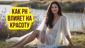Изображение представляет собой цветную фотографию, на которой изображена женщина, сидящая на траве возле водоема. Стиль фотографии естественный и откровенный, она запечатлена в безмятежной обстановке на открытом воздухе. У женщины длинные темно-каштановые волосы и кожа от светлого до среднего оттенка. На ней струящееся прозрачное белое платье со свободными рукавами, которое контрастирует с окружающей природой. Выражение ее лица расслабленное, и она нежно улыбается. На заднем плане видны фиолетовые цветы и несколько сухих растений, которые добавляют колорита этой сцене. Вода спокойна, в ней отражается ясное небо над головой. Общая композиция сбалансирована, объект расположен немного не по центру, что создает гармоничную и умиротворяющую атмосферу.