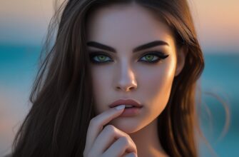 Изображение представляет собой портретную фотографию в высоком разрешении, на которой изображена молодая женщина, женская сексуальность, со светлой кожей и выразительными чертами лица. Ее длинные темно-каштановые волосы ниспадают каскадом на плечи, частично закрывая лицо. У нее пронзительные зеленые глаза, подчеркнутые темной подводкой, и четко очерченные брови. Ее губы слегка приоткрыты, а правая рука нежно касается нижней губы, придавая ей задумчивое выражение. Фон слегка размыт, с градиентом синих и теплых тонов, что наводит на мысль о закате или восходе солнца. Освещение подчеркивает черты ее лица, создавая мягкое сияние вокруг волос и плеч, усиливая общее настроение образа.